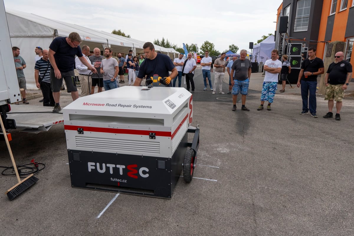 Ukázka opravy vozovky mikrovlnnou technologií v kruhu přihlížejících návštěvníků