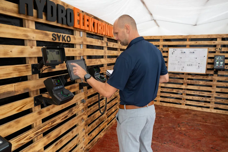 Muž v tmavém poloshirtu ovládá dotykový displej mezi joysticky na dřevěné stěně stánku Hydro Elektronik