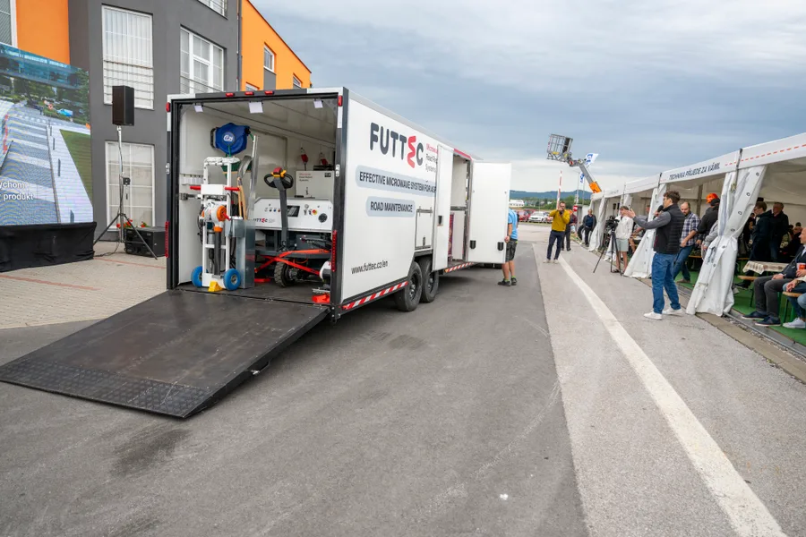 Návěs s mikrovlnnou technologií na opravy vozovek s vyklopenou nájezdovou rampou, vpravo divácký stan