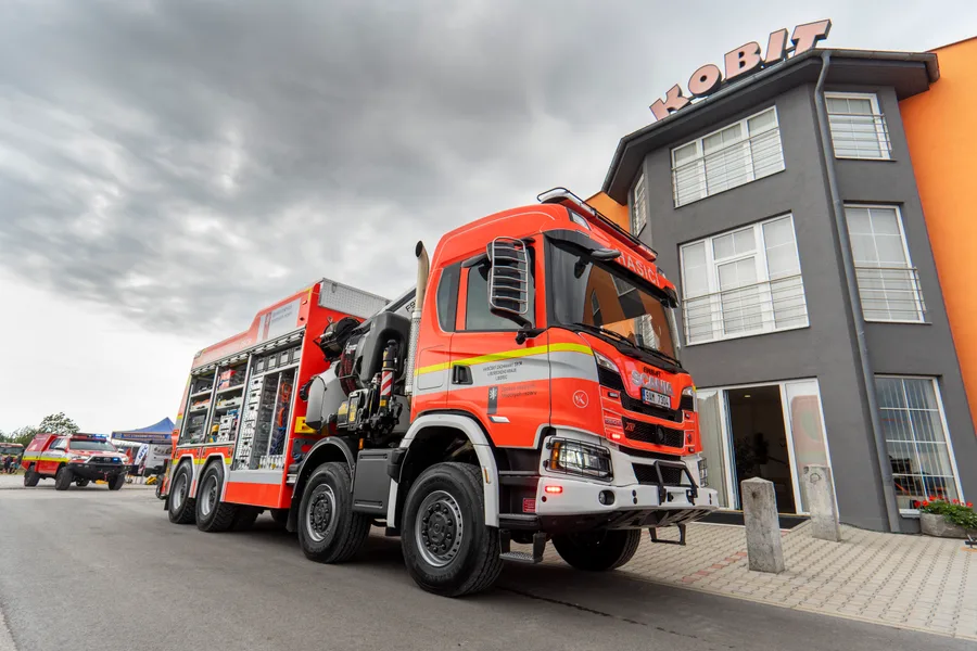 Červená hasičská cisterna na čtyřnápravovém podvozku Scania stojí před budovou s nápisem KOBIT