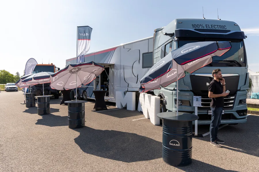Elektrický tahač MAN s nápisem 100% ELECTRIC a předváděcí návěs se slunečníky na asfaltové ploše