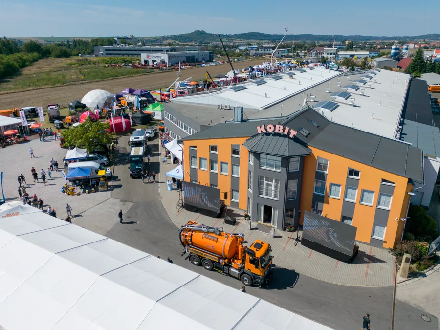 Oranžový vůz s válcovou cisternovou nástavbou stojí před budovou KOBIT, u vchodu dvě LED obrazovky