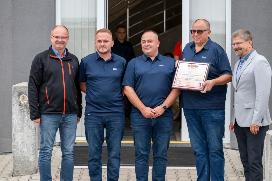 Skupina lidí před vchodem do budovy, jeden z nich drží zarámovanou plaketu s číslicí 30